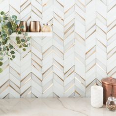 a kitchen counter with gold and white tiles on the wall, potted plant next to it