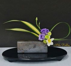 a black plate topped with a flower vase filled with purple and yellow flowers on top of it