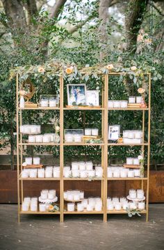 a wooden shelf filled with candles next to a lush green bush covered in leaves and flowers