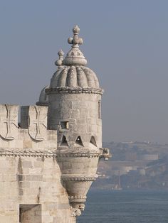 an old stone building with a clock on it's face next to the ocean