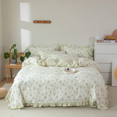 a bed with white comforter and pillows in a room next to a plant on the floor