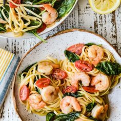 two plates of shrimp pasta with spinach and tomatoes