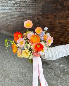 a woman holding a bouquet of flowers in her hand on the sidewalk next to a brick wall