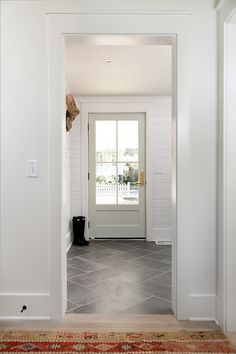 an entryway with white walls and tile flooring is seen from the hallway to the front door