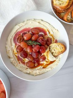 a white bowl filled with mashed potatoes and fruit on top of a table next to bread