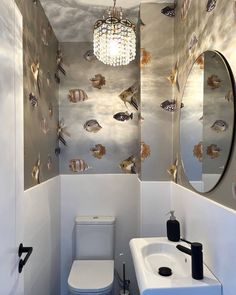 a white toilet sitting next to a bathroom sink under a round mirror on top of a wall