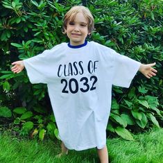 a young boy standing in the grass wearing a white shirt that says class of 2012