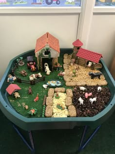 a green tray filled with fake farm animals and hay in front of a window on the floor