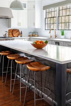 a large kitchen island with four stools and a bowl of fruit on the counter