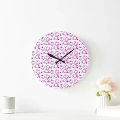 a clock with pink and blue designs on it next to a white vase filled with flowers