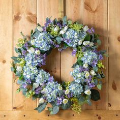 a wreath with blue and white flowers hanging on a wooden wall