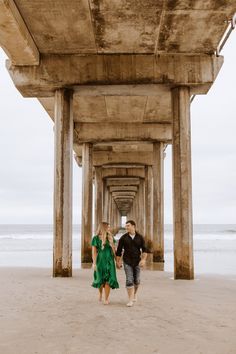 a man and woman walking under a pier on the beach