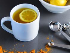 there is a cup of tea and spoons next to the bowl with lemon slices on it