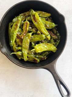 cooked green peppers in a frying pan on a white counter top with tongs