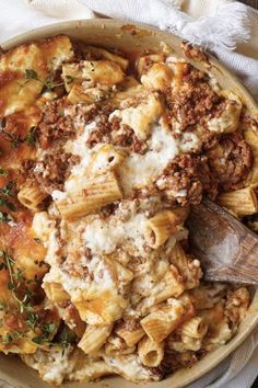 a bowl full of pasta with meat and cheese on the top, next to a wooden spoon