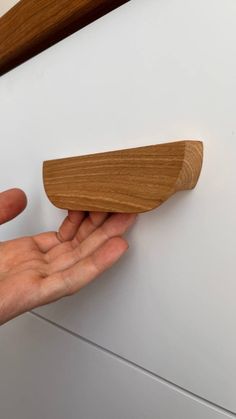 a hand holding a wooden object in front of a white wall with wood trimming