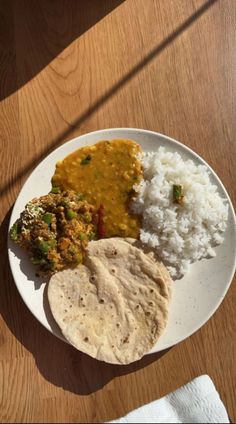 a white plate topped with rice, meat and veggies on top of a wooden table