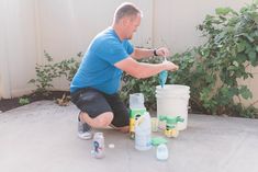 a man sitting on the ground next to several buckets and paint bottles in front of him