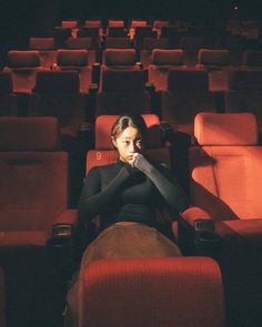 a woman is sitting in an empty theater with her hand on her chin and looking off to the side