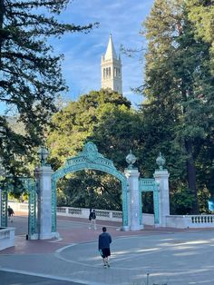 a person walking in front of an arch with a clock tower in the back ground