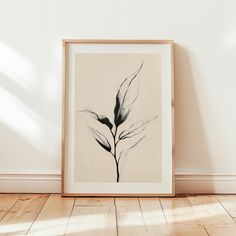 a black and white photo of a plant in a frame on the floor next to a wall