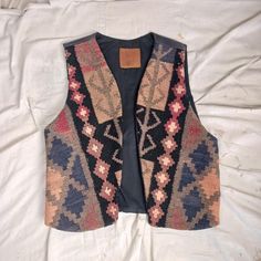 Beautiful vest made with thick wool on the front and black leather on the back. The wool is like a tapestry with a great design and use of colors. The back is a soft black leather. There is a black liner with a single pocket on the inside left. Condition is very good. No holes or rips or stains. Clean and ready to go.  No makers mark or size designation. Measurements: Armpit to armpit  18 inches Shoulder to shoulder   14 3/4 inches Length, from rear collar seam to end of vest   20 inches Winter Bohemian Black Vest, Black Folk Style Festival Vest, Tapestry Vest, Puffer Jacket Men, Wool Tapestry, Grand Junction, Western Boots Women, Thick Wool, Black Liner