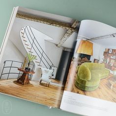 an open book showing a living room with green couches and stairs in the background