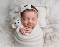 a newborn baby wrapped in a white blanket with a teddy bear on it's side