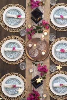 the table is set with blue and white plates, silverware, and pink flowers