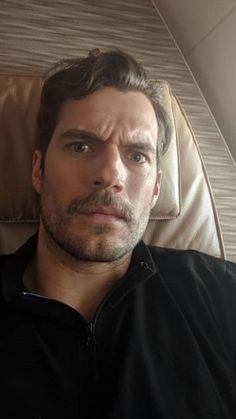 a man is sitting in an airplane with his eyes closed and looking at the camera