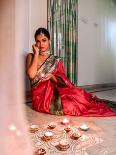 a woman in a red sari sitting on the floor next to candles and talking on her cell phone