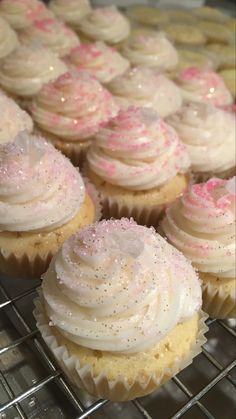 cupcakes with white frosting and pink sprinkles are on a cooling rack