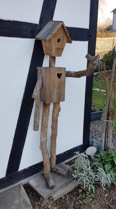 a wooden sculpture of a man holding a birdhouse in his hand and standing next to a house