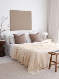 a bed with white sheets and pillows in a bedroom next to a painting on the wall