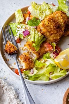 a white plate topped with meat and salad next to a fork on top of a table