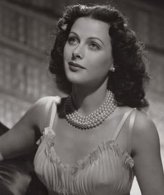 an old black and white photo of a woman with pearls on her neck wearing a dress