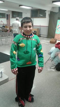 a young boy wearing a green christmas sweater and black pants standing in an empty room