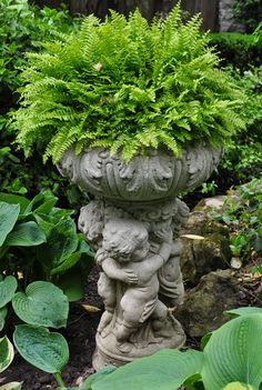 a planter in the middle of a garden filled with green plants and other greenery