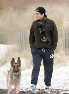 a man standing in the snow with his german shepard dog on a leash next to him