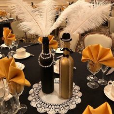 the table is set with black and white plates, silverware, champagne bottles, and feathers