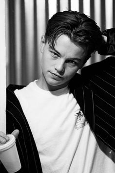 black and white photograph of a young man in a suit leaning against a wall with his hand on his head