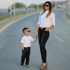 a woman standing next to a little boy on the side of a road holding hands