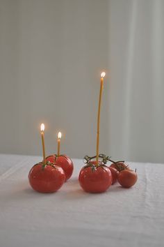 three tomatoes with candles sticking out of them sitting on a white tablecloth covered surface