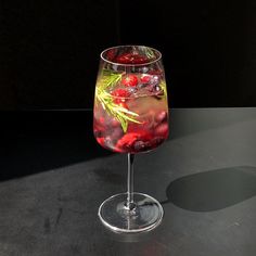 a glass filled with liquid and berries on top of a black table next to a wall