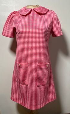 This pink gingham dress is so dreamy! It is handmade and from the 1960's, so totally one of a kind and in fantastic condition with no known flaws! It is closest to a size medium, but here are the exact measurements taken lying flat and doubled: Shoulders: 13 inches Chest: 36 inches Waist: 34 inches Hips: 36 inches Shoulders to Hem: 34 inches This dress is made from polyester and zips up the back to close. It has sweet little buttons on the front facing pockets. The collar is a Peter Pan style, r Retro Gingham Plaid Dress For Spring, Retro Gingham Dress For Spring, Retro Gingham Plaid Spring Dress, Retro Plaid Dress For Spring, Vintage Gingham Plaid Dress With Short Sleeves, Vintage Style Gingham Plaid Short Sleeve Dress, Spring Vintage Gingham Plaid Dress, Vintage Plaid Dress For Spring Picnic, Fitted Vintage Plaid Dress For Spring