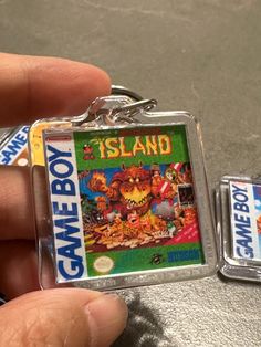 a hand holding a game boy keychain that is in front of another key chain