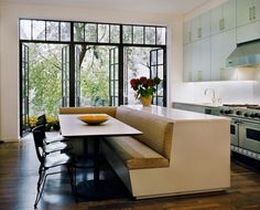 a kitchen with an oven, table and chairs next to a window that looks out onto the woods