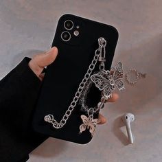 a person holding an iphone case with two charms attached to it, while another phone is next to them