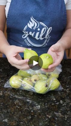 a person holding some green apples in their hands on a counter top with a bag of them