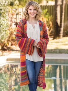 a woman standing next to a pool wearing a multicolored knitted cardigan